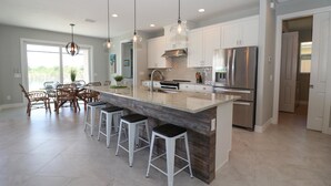 Una cocina amplia con una isla grande, electrodomésticos modernos y un comedor con sillas de mimbre.