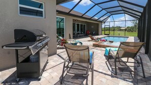 Un patio techado con una parrilla, sillas de descanso y una piscina.