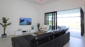 Ein modernes Wohnzimmer mit einem schwarzen Ledersofa, einer weißen Unterhaltungsanlage und einem großen Fernseher, der eine schöne Aussicht zeigt.