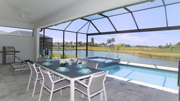 Ein Essbereich mit Tisch für vier Personen, mit Blick auf einen Pool und eine Aussicht auf Golfplatz und Wasserfläche.