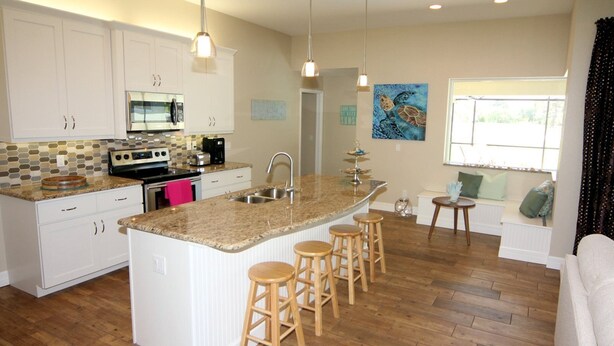 A modern kitchen with white cabinets, a granite countertop, a built-in oven, and a large island with stools. - Lazy Gator (Rotonda West)