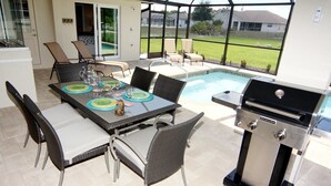 An outdoor patio with a dining table set for four, surrounded by wicker chairs. A grill is positioned to the right of the table. - Lazy Gator (Rotonda West)
