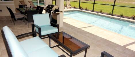 An outdoor patio area with a pool, seating, and a grill.