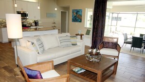 A modern living room with a white sofa, wicker chairs, a wooden coffee table, and a kitchen in the background. - Lazy Gator (Rotonda West)