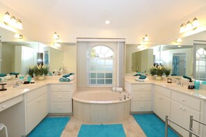 A bathroom with a large bathtub, two sinks, and a large mirror. There are towels and toiletries on the counter. - Suntastic (Rotonda West)