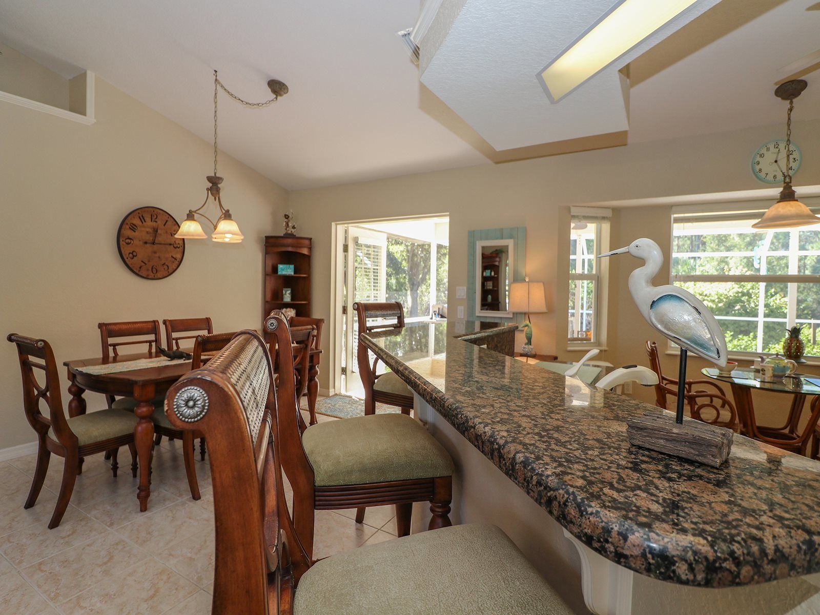 A kitchen with a granite countertop, wooden chairs, a dining table, and a large window with a view.