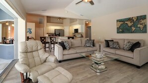 A spacious living room with a glass coffee table, beige sofas, and a ceiling fan.