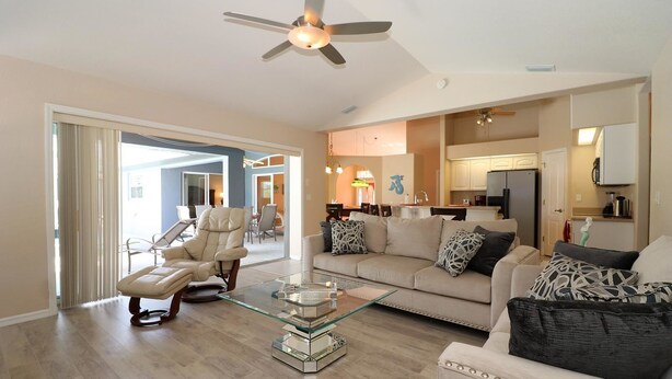 A spacious living room with a glass coffee table, a leather recliner, and a beige sofa with patterned cushions.