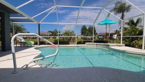 A pool area with a clear blue pool, a white metal roof structure, and a turquoise umbrella.