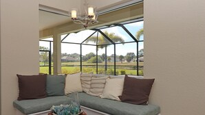 A cozy seating area with a bench and cushions, a woven side table, and a view of a green landscape through a large window. - Blue Pearl (Rotonda West)