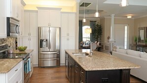 A modern kitchen with stainless steel appliances, a large island with a sink, and a dining area in the background. - Blue Pearl (Rotonda West)