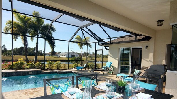 A covered outdoor patio with a pool, lounge chairs, and a dining table set for six. - Blue Pearl (Rotonda West)