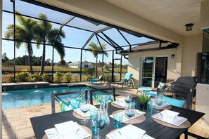 A covered outdoor patio with a pool, lounge chairs, and a dining table set for six. - Blue Pearl (Rotonda West)