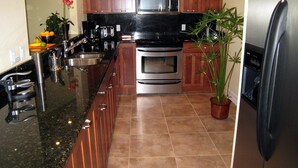 A modern kitchen with wooden cabinets, stainless steel appliances, a granite countertop, and a potted plant. - Happy Days at Alhambra (Port Charlotte)