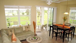 A living room with a sofa, coffee table, dining table, chairs, and large windows. - Happy Days at Alhambra (Port Charlotte)