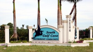 A sign for South Gulf Cove Waterfront Community with a bird silhouette, palm trees, and a gated entrance. - Dolphin Cove (Port Charlotte)