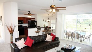 A modern living room with a black leather sofa, a glass coffee table, and a dining area with a pool view. - Dolphin Cove (Port Charlotte)