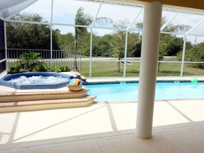 A swimming pool with a hot tub and lounge chairs, surrounded by a glass enclosure with a view of greenery. - Coastal Breeze (Rotonda West)