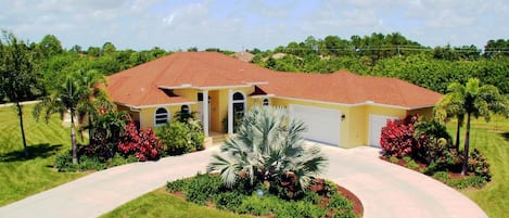 A single-story house with a red-tiled roof, a yellow facade, and a driveway leading to a garage.