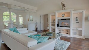 A spacious living room with a white leather sofa, a glass coffee table, and decorative items on shelves.