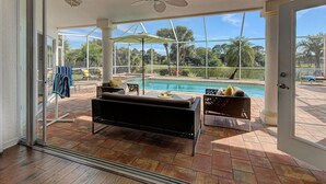 A sunlit patio with a pool, outdoor seating, and a view of a lush garden.