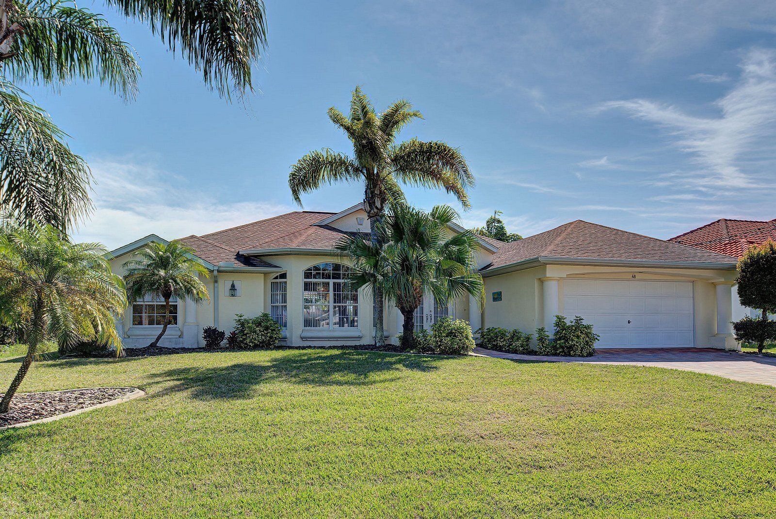 A two-story house with a well-maintained lawn and palm trees.