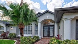 A two-story house with a central entrance, a covered porch, and a large palm tree.