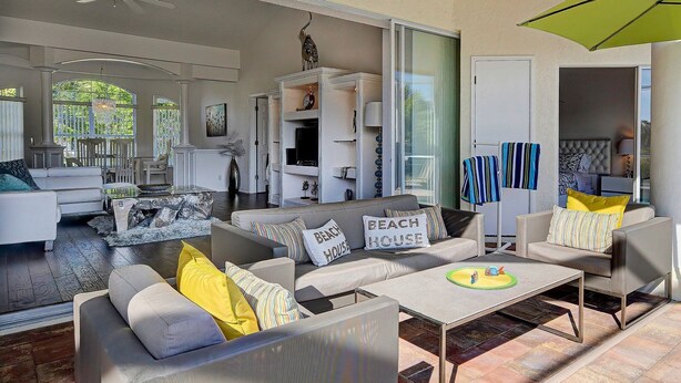 A spacious living area with a sofa set, a coffee table, and a TV. There is a sliding door leading to a bedroom.