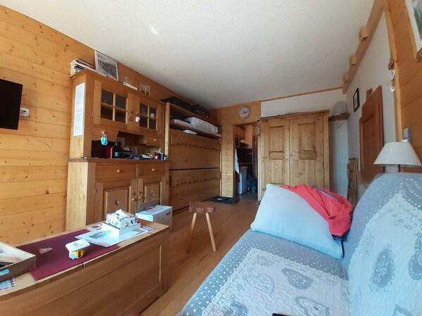 Ein gemütliches Zimmer mit Holzwänden, einer Couch, einem kleinen Tisch mit Gegenständen und einer Küchenzeile mit Schränken und einer Mikrowelle.