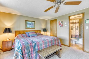 A bedroom with a bed, bedside lamps, a ceiling fan, a wooden bench, a door, and a bathroom visible through an open door. - Townhouse-style condo on golf course w/ open living room and balcony (Sugar Mountain)