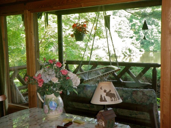 Een houten terras met een tafel, stoelen, een lamp en een hangende bloempot.