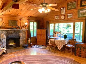 Ein Interieur einer Holzhütte mit Kamin aus Stein, Esstisch, Stühlen und Deckenventilator.