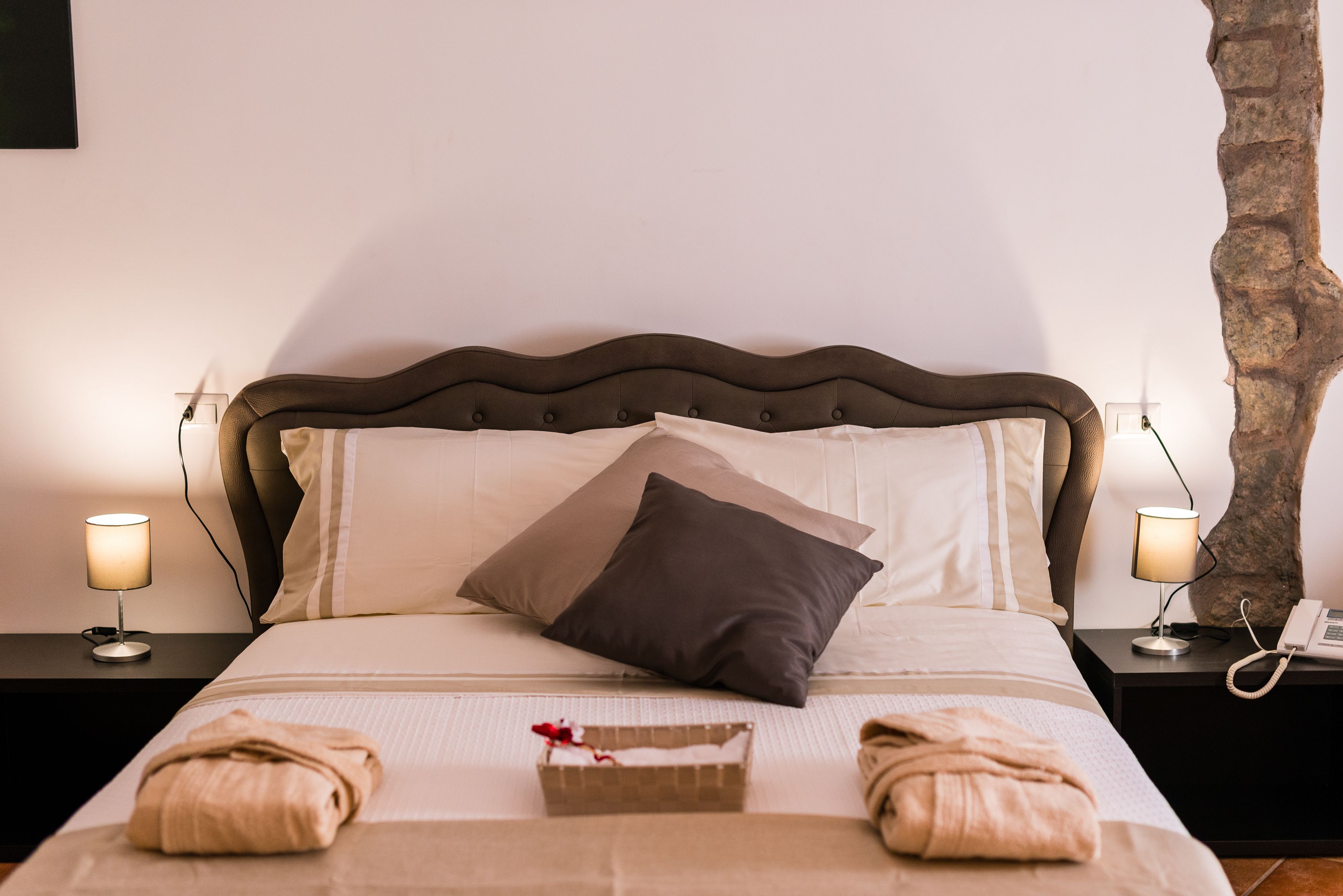 Un letto rifatto con precisione, con una testiera marrone, due lampade ai lati del letto e un telefono sul comodino.