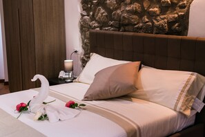 A neatly made bed with a swan and roses, a stone wall, and a bedside table with a lamp and phone. - Le Undici Rose Hotel (Viterbo)