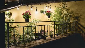 A balcony with hanging plants and a chair, overlooking a garden with bamboo and flowering plants. - Le Undici Rose Hotel (Viterbo)