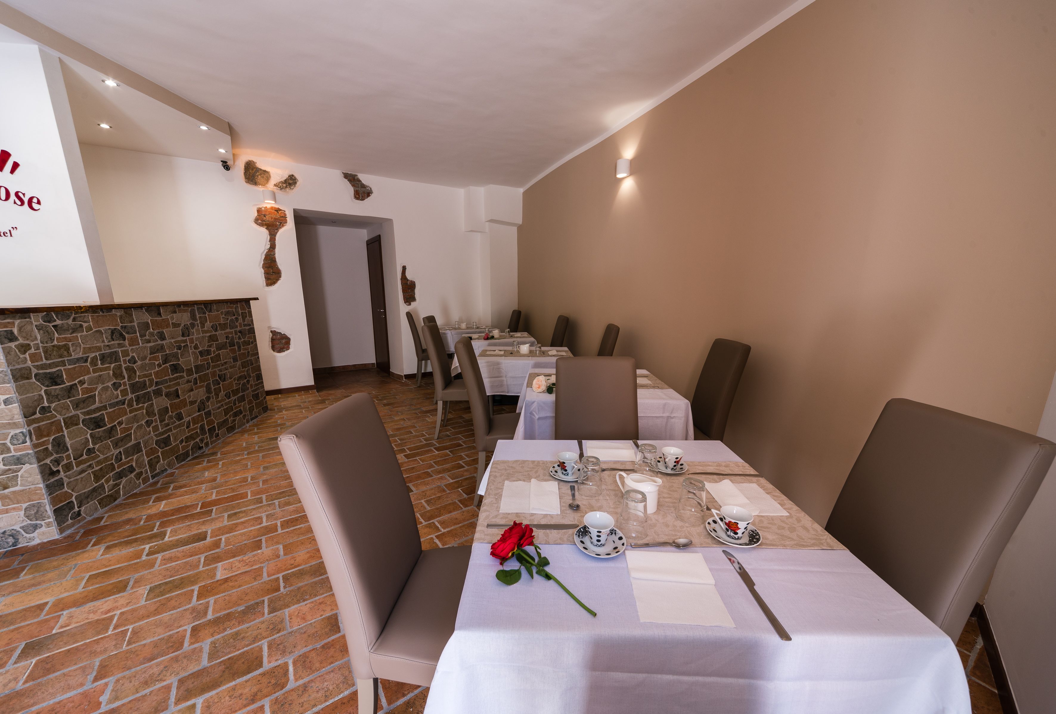 Un espace repas avec un sol en briques, des tables blanches et des chaises marron.