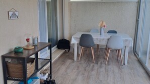 Una zona patio coperta con tavolo e sedie, un piccolo ripiano con oggetti e vista sugli alberi attraverso le porte vetrate.