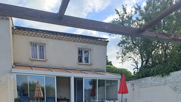 Una piscina con bordo in pietra, un portico coperto con mobili da esterno e una casa con tetto in tegole.