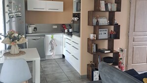 Una cucina moderna con mobili bianchi, un forno a microonde integrato e una macchina da caffè. C'è un'area pranzo con un tavolo bianco e un divano grigio.