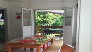 Een eetgedeelte met een tafel met glazen blad, een houten bank en gestreepte kussens.