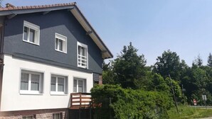 Een woonhuis met twee verdiepingen, een witte gevel en donker dak, omgeven door groen.