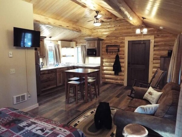 A log cabin interior with a kitchen, dining area, and living room.