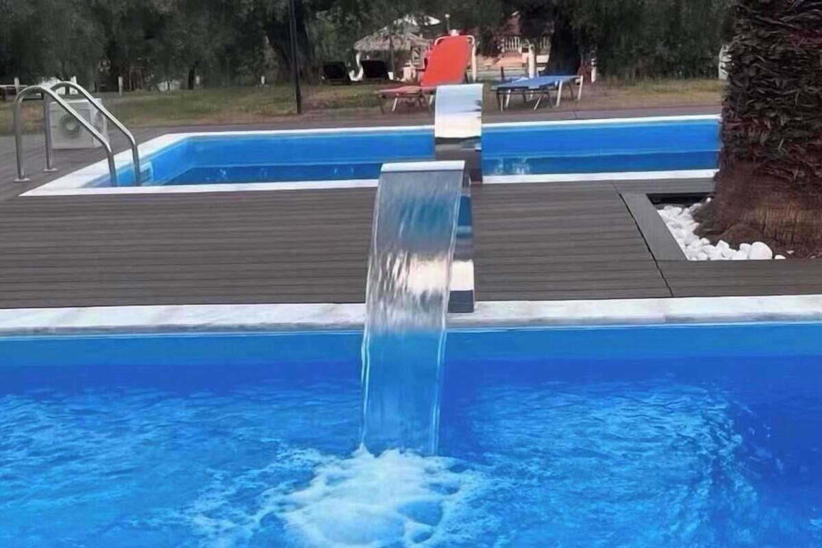 Une piscine agrémentée d’une cascade, entourée d’une terrasse en bois et d’un palmier.