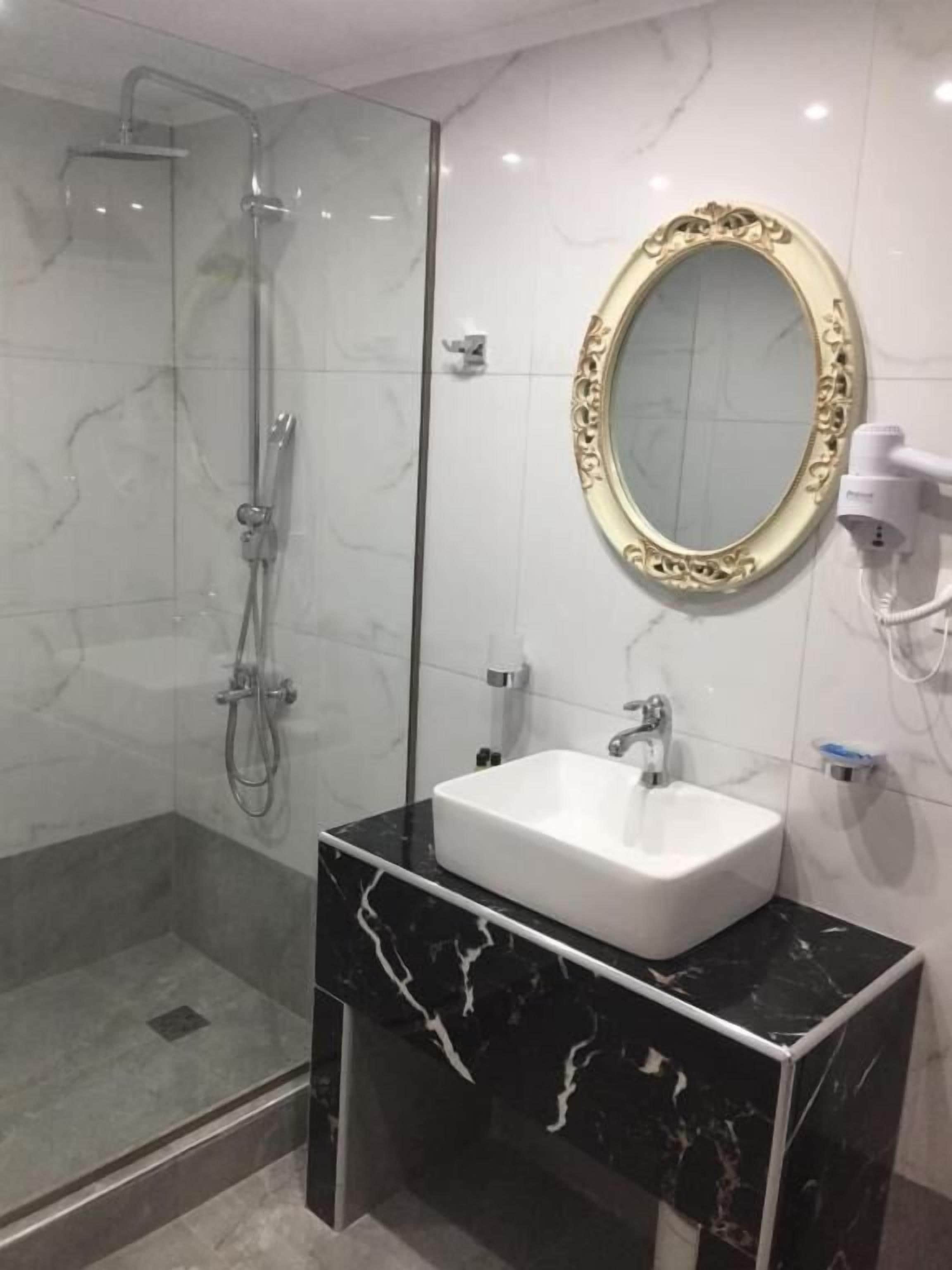 A modern bathroom with a glass-enclosed shower, a white sink with a marble countertop, and a gold-framed mirror.