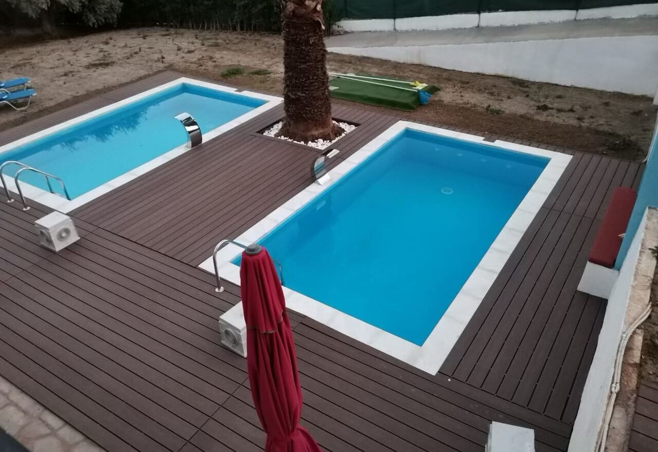 Un espace piscine comprenant deux piscines, une terrasse en bois et un parasol rouge.