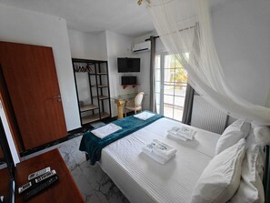 A hotel room with a bed, a desk with a computer, a TV, a wardrobe, and a window with curtains. - Villa Askamnia and Suites (Sithonia)