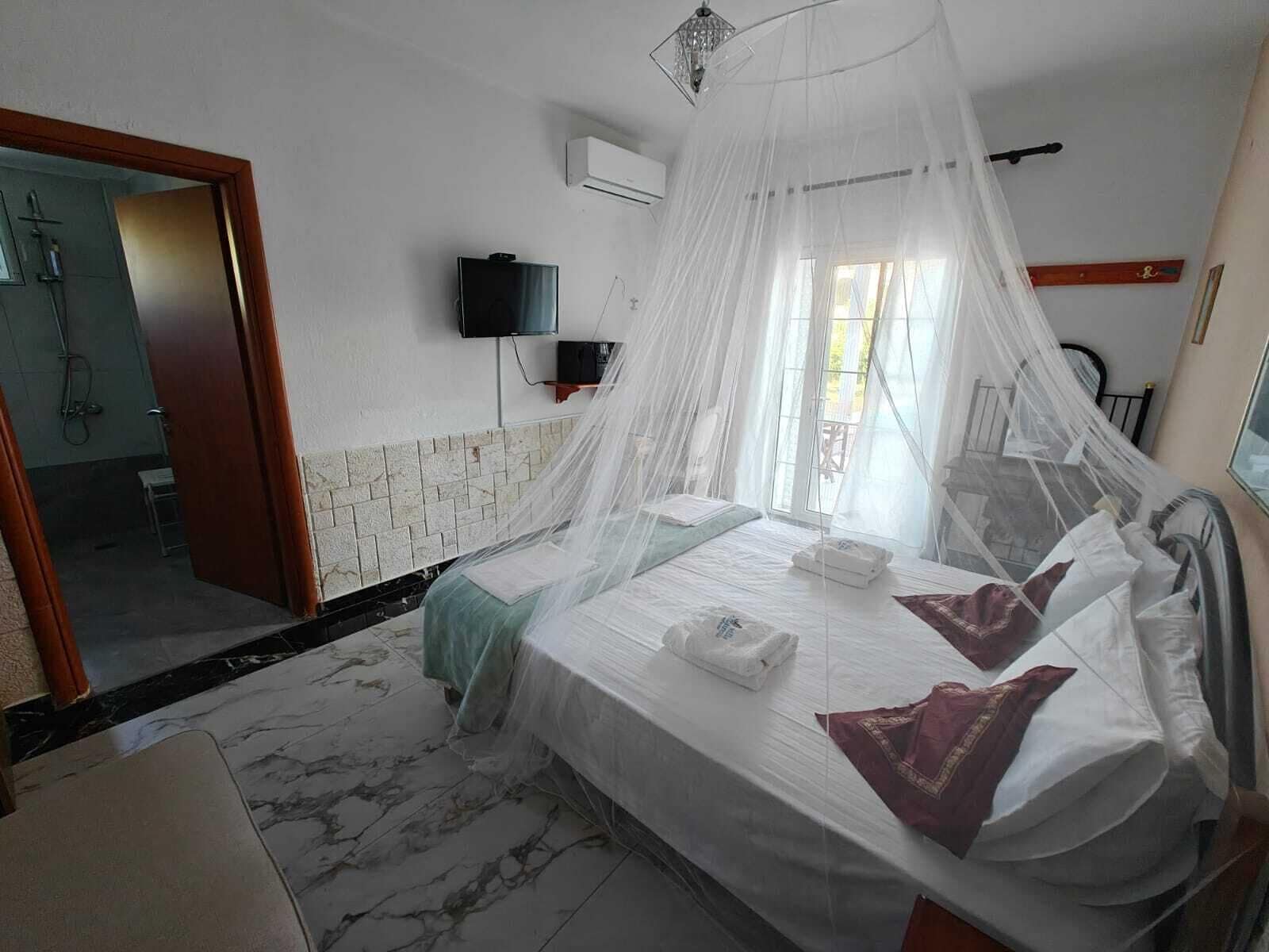 A hotel room with a bed, a TV, a mosquito net, and a bathroom visible through an open door.