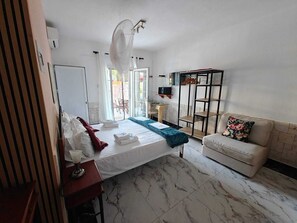 Un dormitorio con cama, sofá, escritorio y balcón.