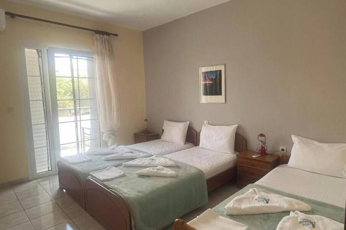 Une chambre d’hôtel avec deux lits, une fenêtre avec des rideaux, un tableau encadré au mur et une petite table avec une lampe.
