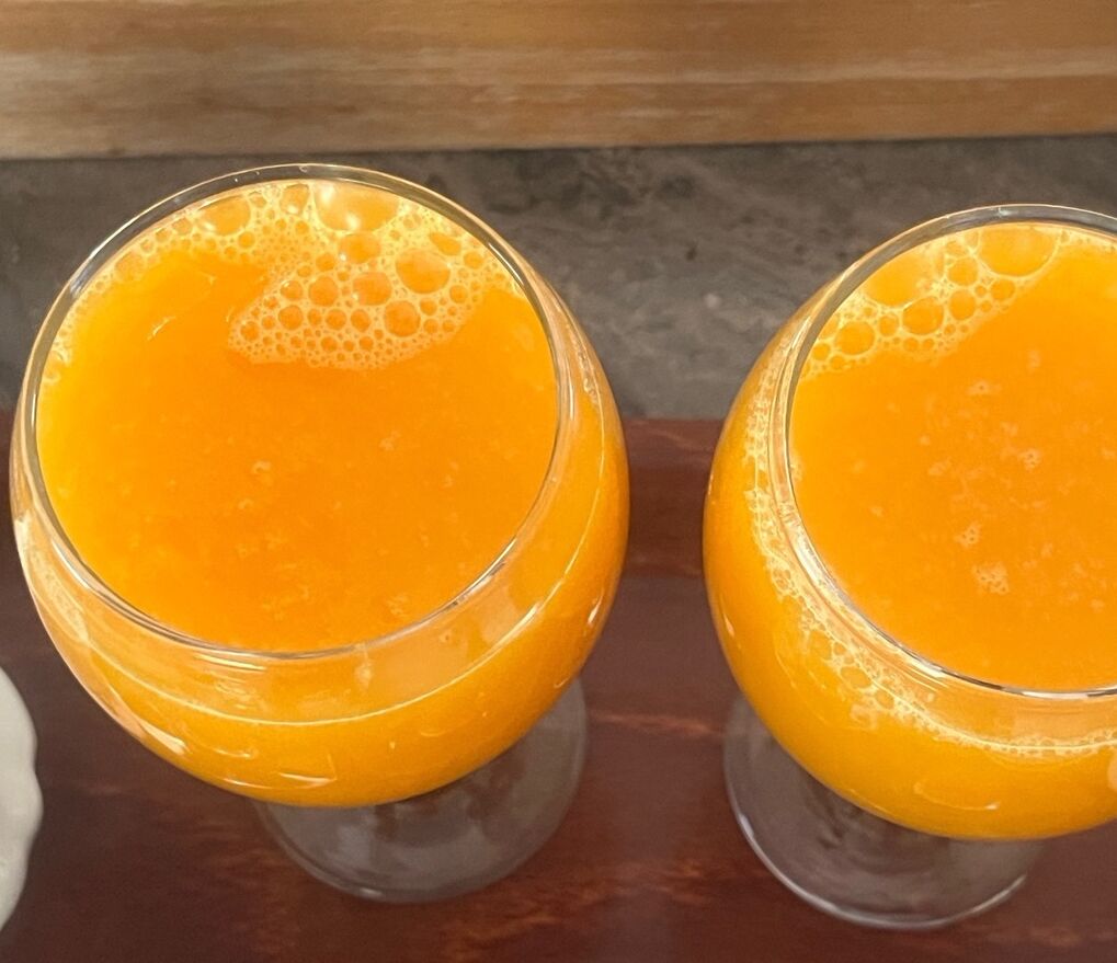 Two glasses of orange juice on a wooden surface.